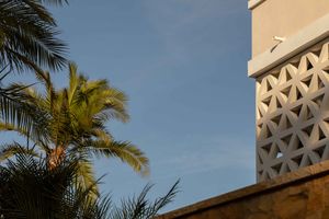 Palm trees sway against a blue sky next to a modern building with decorative lattice pattern detail.