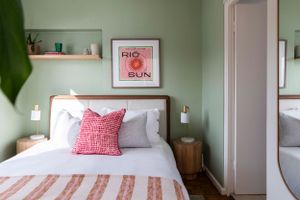 Cozy bedroom with pink accent pillow, striped bedding, and modern wall art against sage green walls.