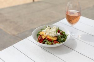 Fresh salad bowl and rose wine glass on white outdoor table.