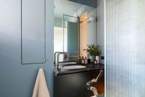 Modern bathroom interior with blue-green walls, mirror, and black vanity.