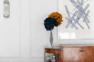 Vintage sideboard with dried flowers beneath abstract wall art and sconce light.