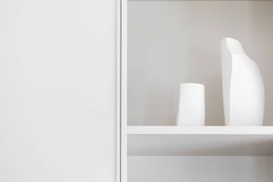 Minimalist white shelf with ceramic vases against neutral wall.