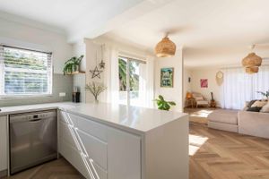 Modern white kitchen with herringbone flooring, built-in seating and natural lighting.