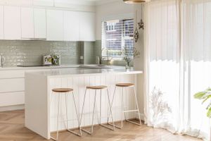 Bright white kitchen featuring minimalist design with bar stools and glass backsplash.
