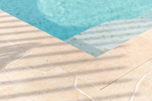 Modern pool edge with geometric shadows casting patterns on light concrete.