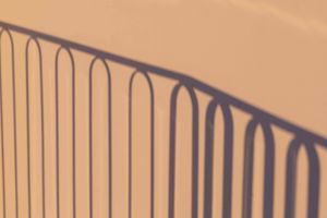 Abstract shadow pattern of curved metal railing against beige wall.