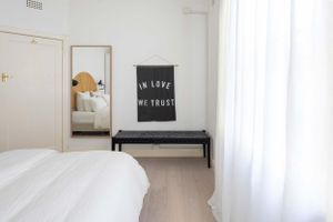 Clean modern bedroom with black bench and 'In Love We Trust' typography art.