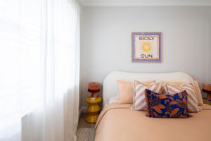 Minimalist bedroom with peach bedding, blue accent pillow, and retro wall art.