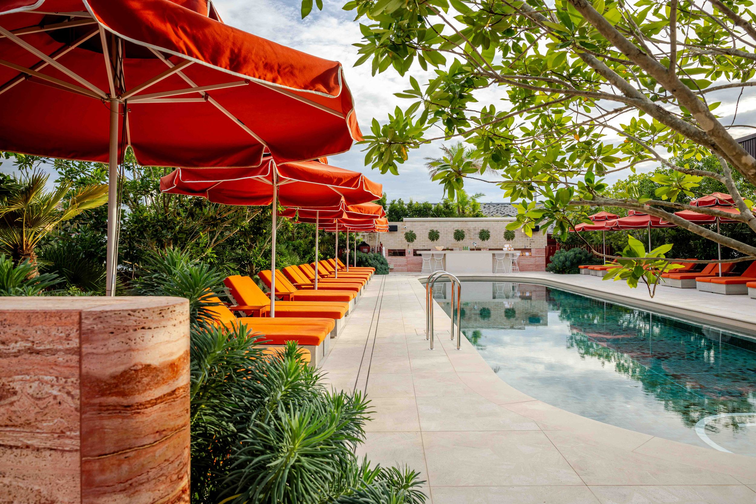 Luxury hotel pool with orange lounge chairs and red umbrellas surrounded by lush tropical greenery.