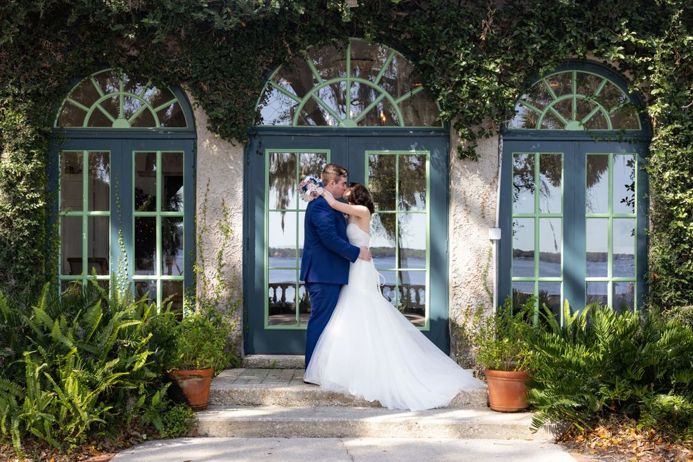 A wedding couple embraces in front of elegant arched French doors at a historic venue.