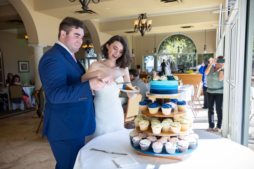 A couple cuts their wedding cake featuring blue and white cupcakes at an elegant reception.