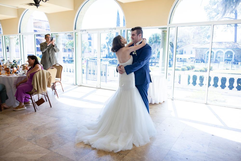 A romantic first dance between newlyweds in a sunlit ballroom with arched windows.