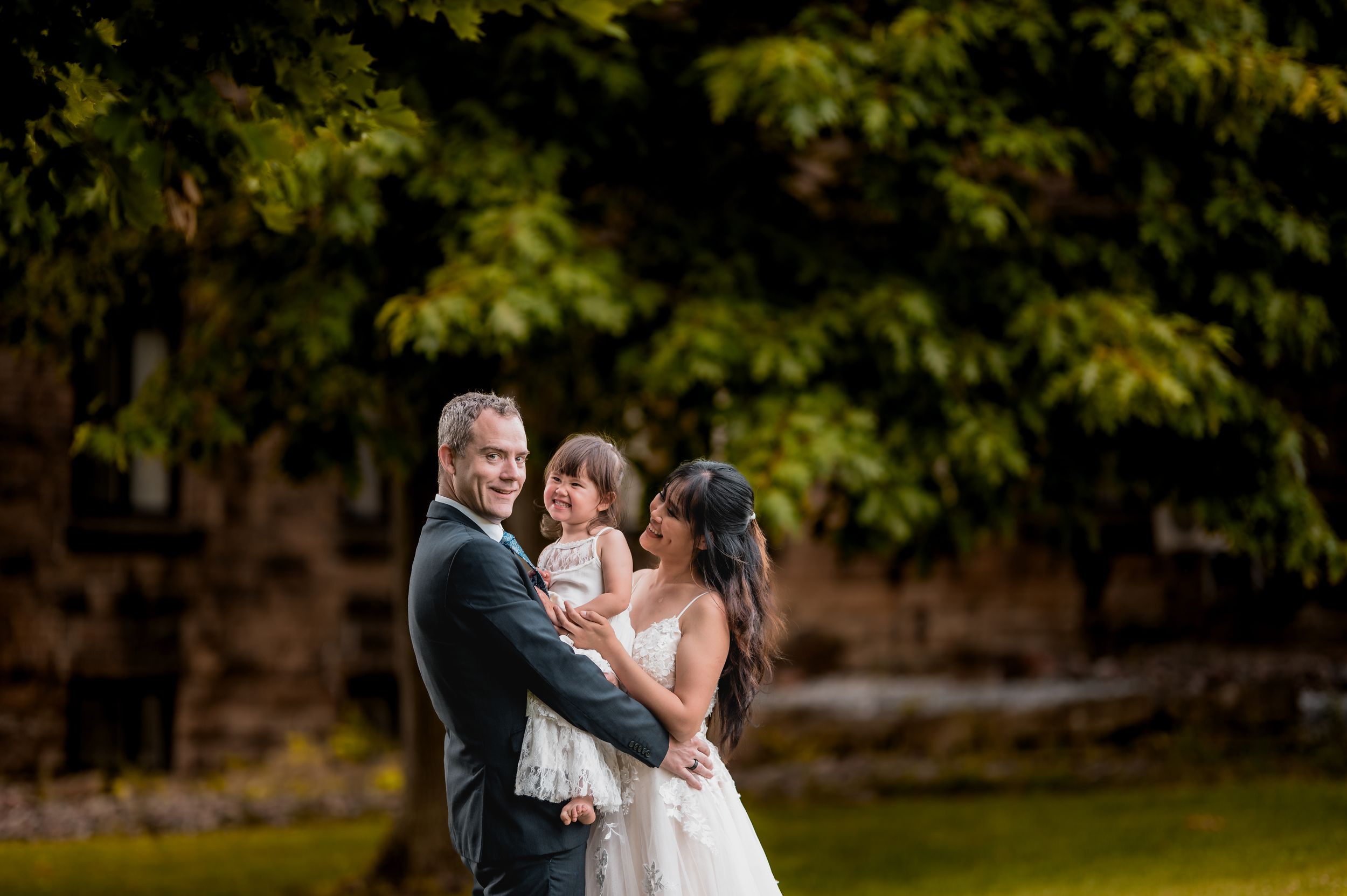 Newlyweds share a romantic moment under green trees in a garden setting. New Brunswick Wedding photographer