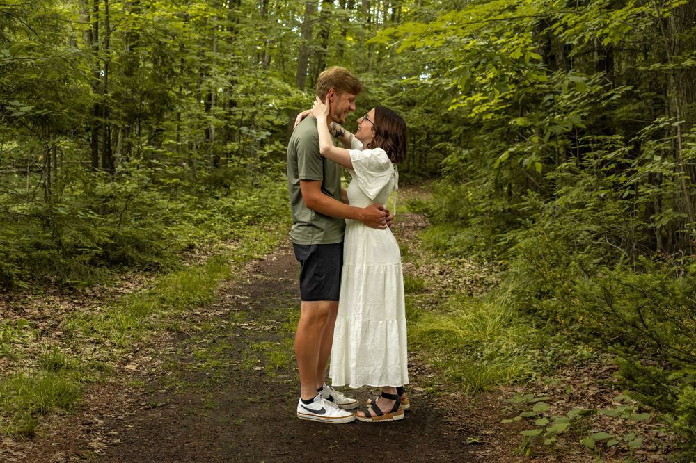 Couple sharing intimate moment on forest trail surrounded by greenery.
