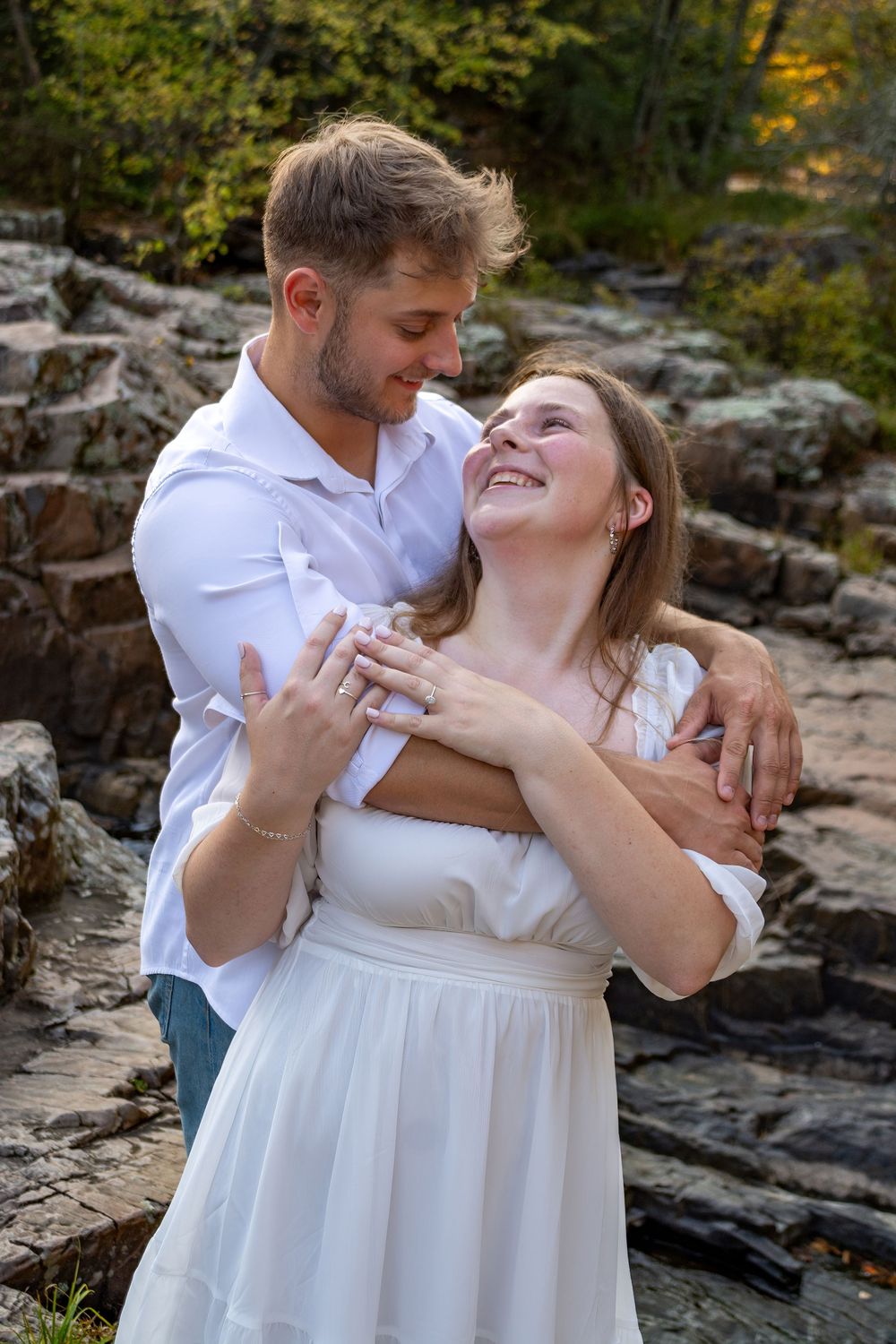 A romantic couple embraces on rocky terrain surrounded by autumn foliage.