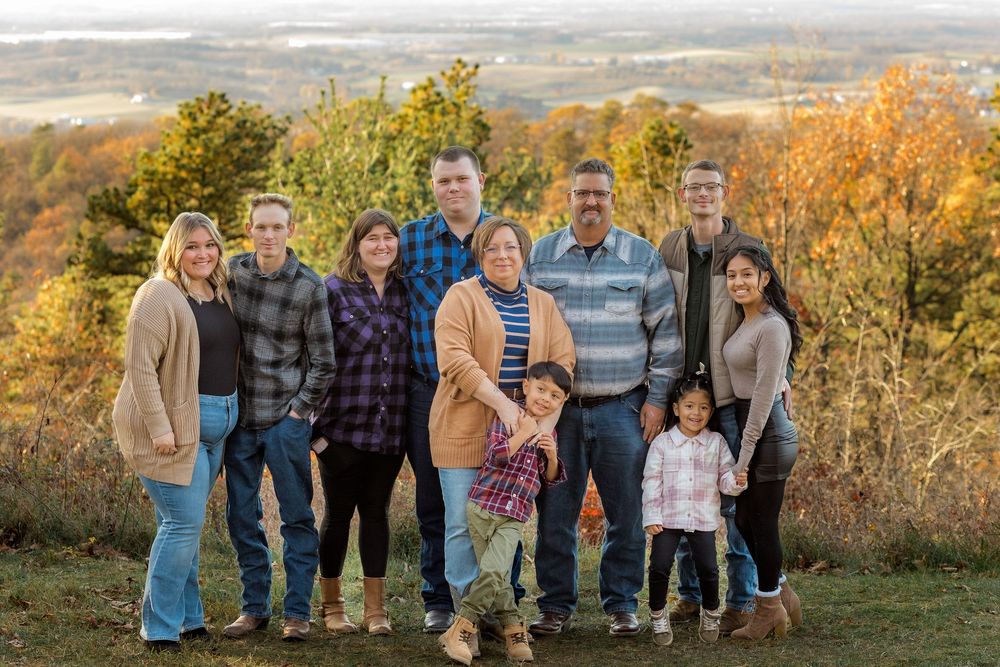 Group stands together on hilltop during golden autumn sunset with rolling landscape in background.