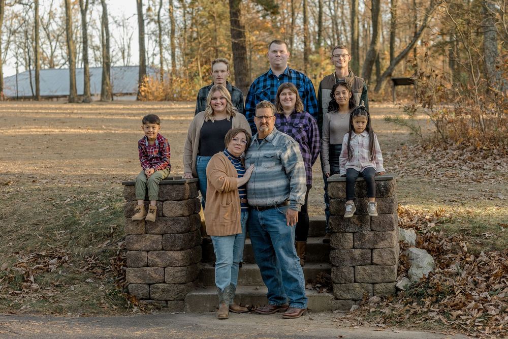 A group of people standing together outdoors by a stone wall in an autumn setting with fallen leaves.