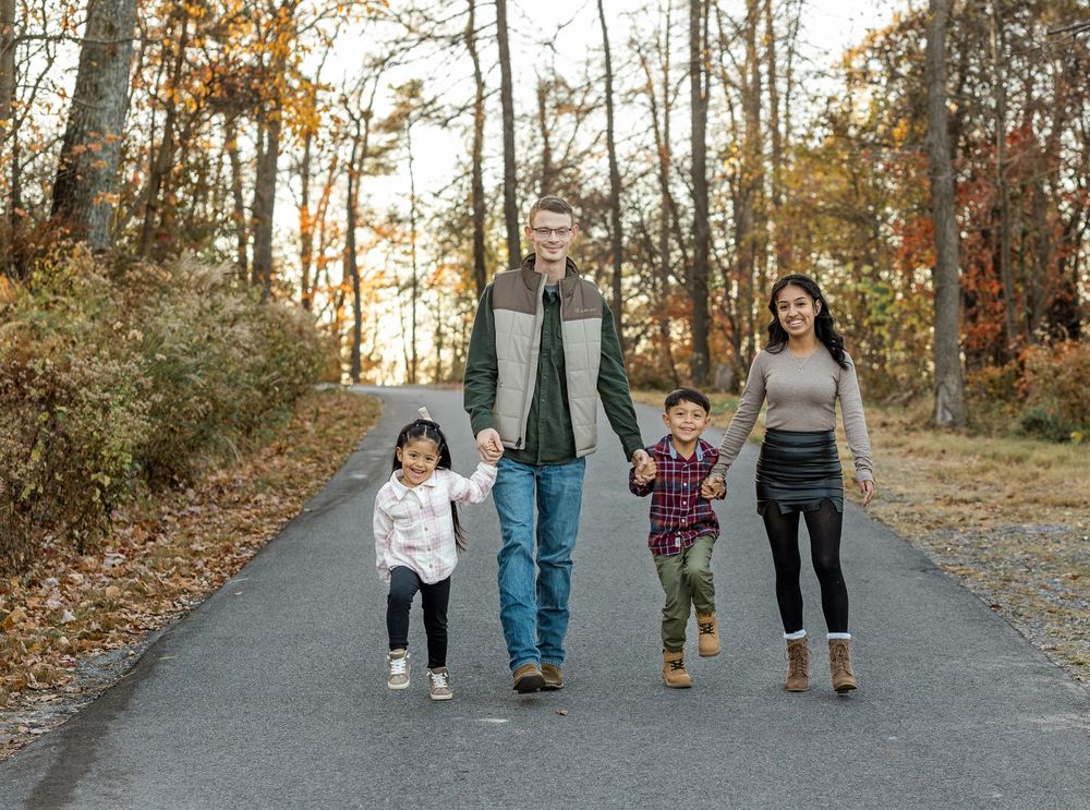 Multiple sets of feet and legs walking on an asphalt path during fall, showing casual shoes and jeans.
