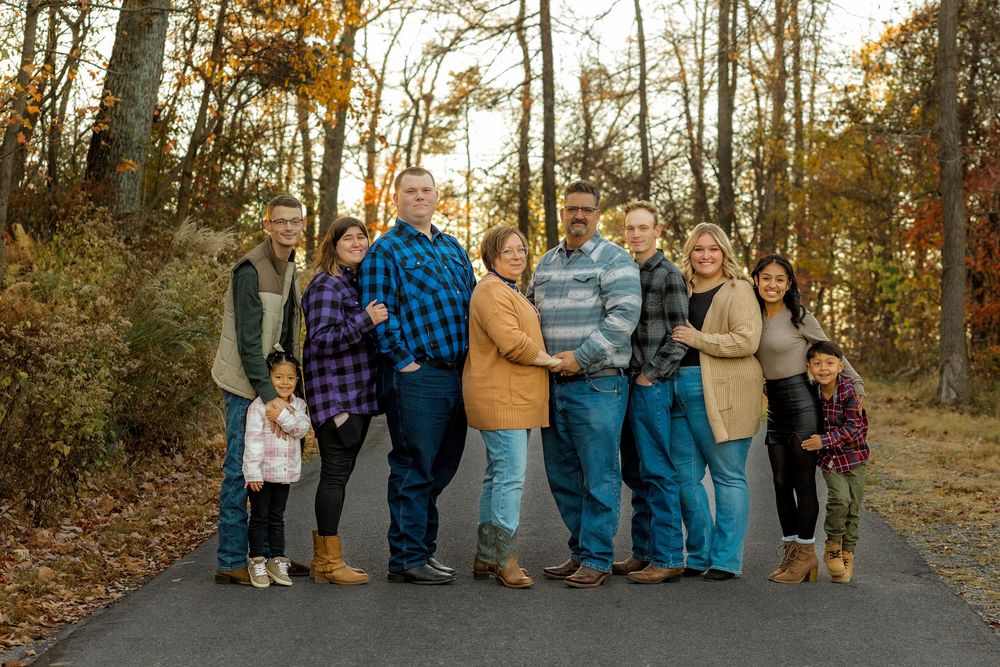 A group of people sitting on outdoor steps surrounded by autumn trees in casual attire at sunset.
