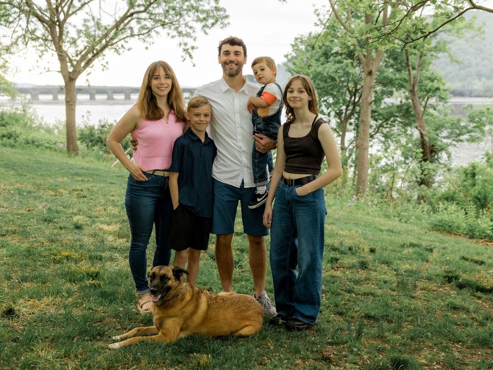 Group enjoying a sunny day together with their German Shepherd dog on a grassy hillside.