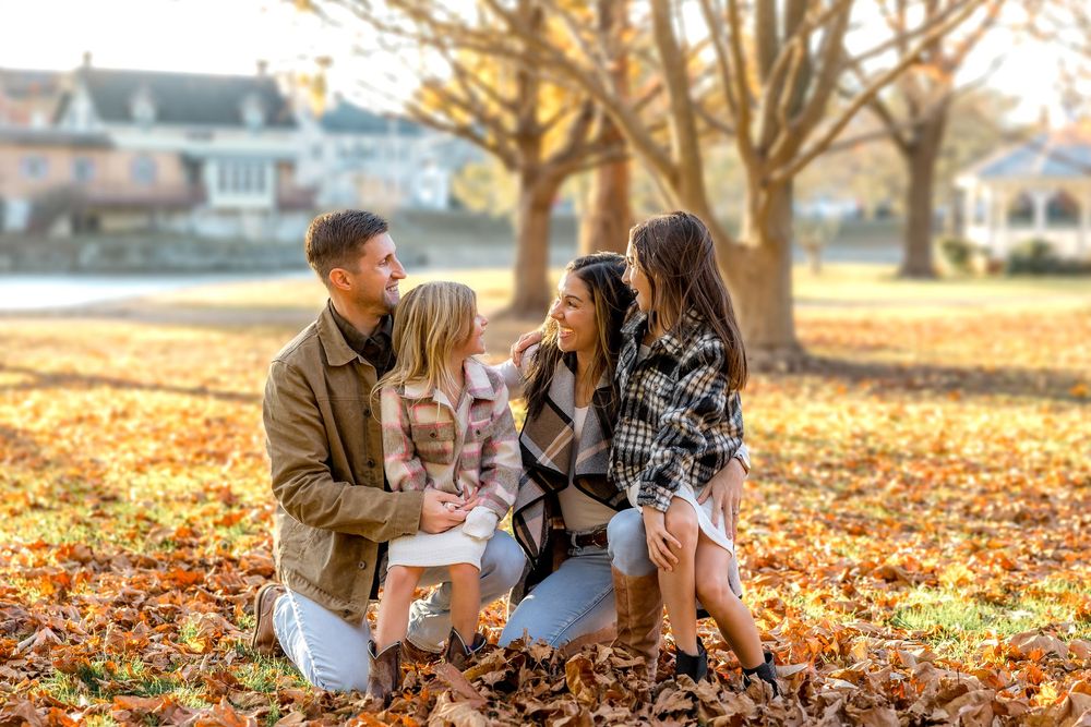 A family plays together in a park on a beautiful autumn day surrounded by golden fallen leaves.