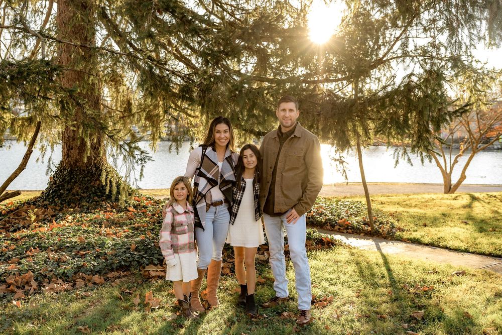 Family group stands together in sun-dappled forest clearing during golden hour sunset.