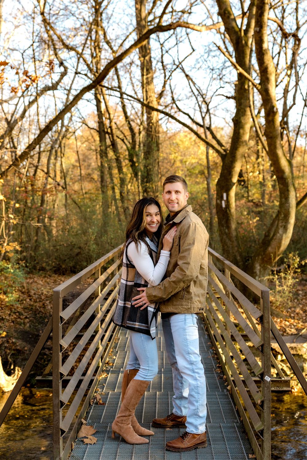 A couple shares an intimate moment on a wooden bridge surrounded by autumn trees in the woods.