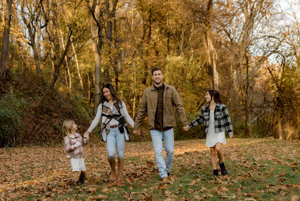 Family walking together through an autumn scene with trees and fallen leaves in the warm sunlight.