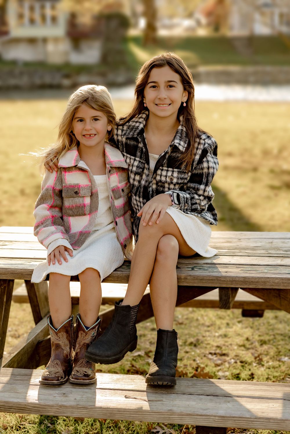 Two children in plaid shirts sitting close together on a rustic wooden bench during golden hour.
