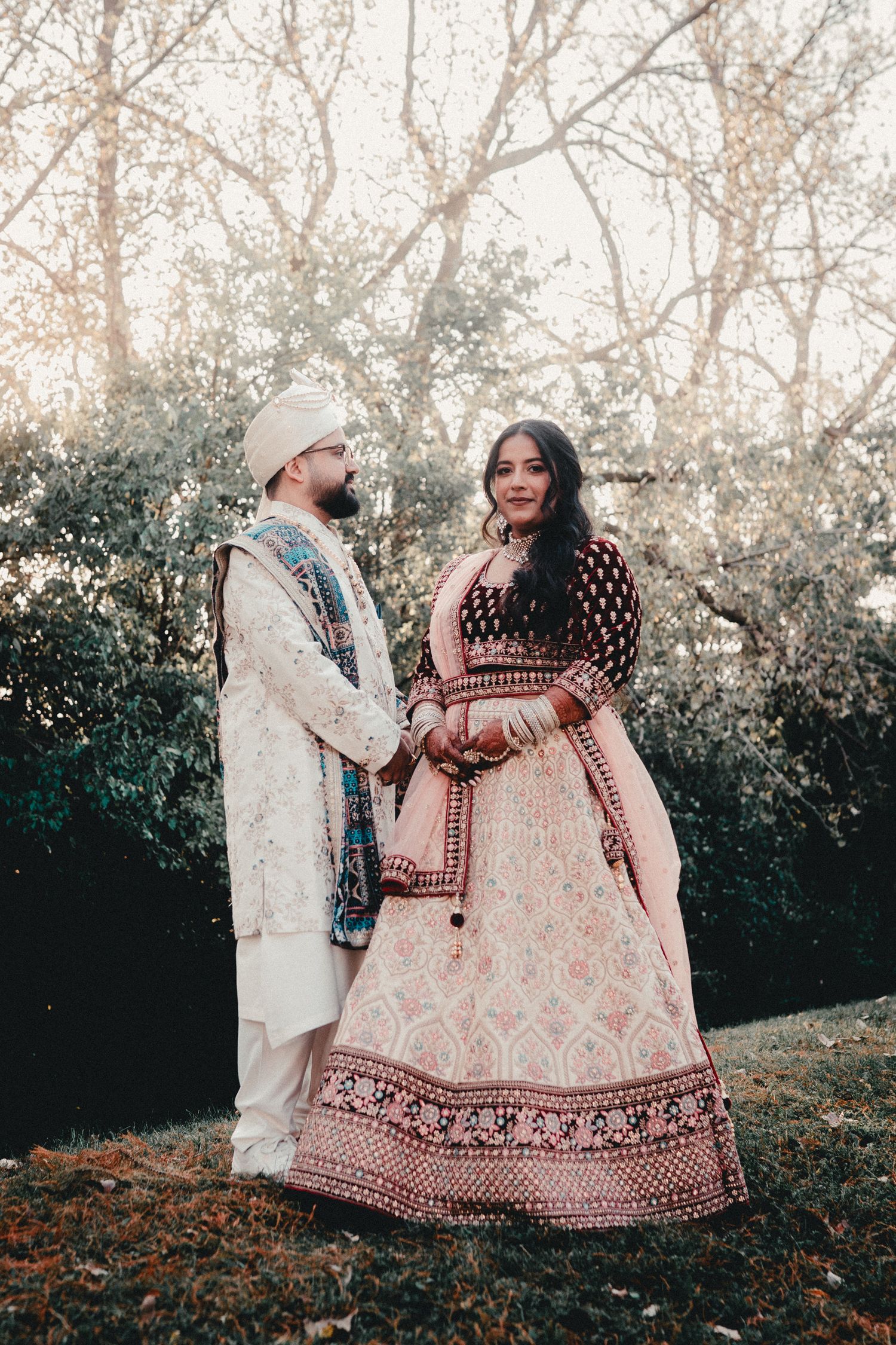 A couple in traditional Indian wedding attire standing together in an autumn setting. Indian Wedding Photography Toronto GTA