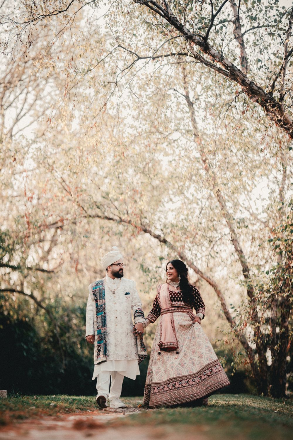 A couple in traditional Indian wedding clothes walking under blossoming trees. Indian Wedding Photography Toronto GTA