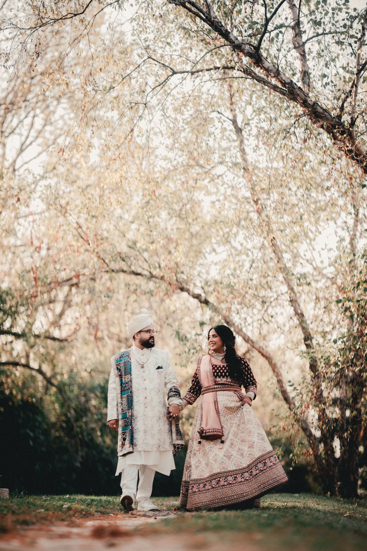 A couple in traditional Indian wedding clothes walking under blossoming trees. Indian Wedding Photography Toronto GTA