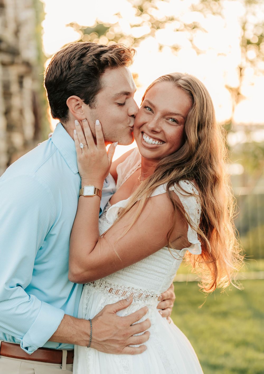 A loving couple shares a romantic moment outdoors during golden hour while dressed in white and light blue outfits.