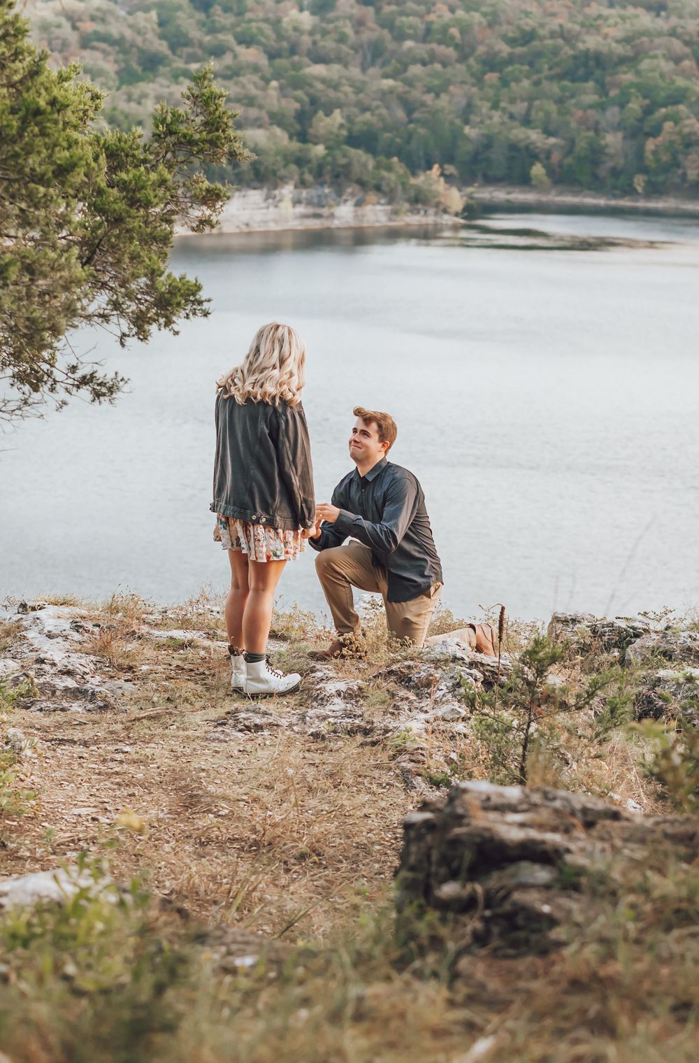 A romantic proposal moment captured at a scenic lakeside overlook surrounded by autumn trees and wilderness.