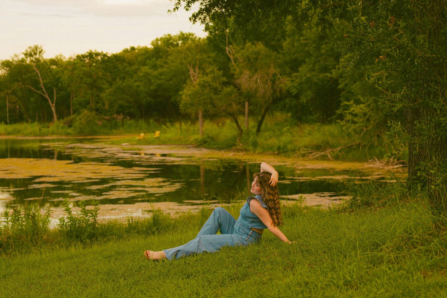 Person relaxing on grass near a scenic lake during sunset.
