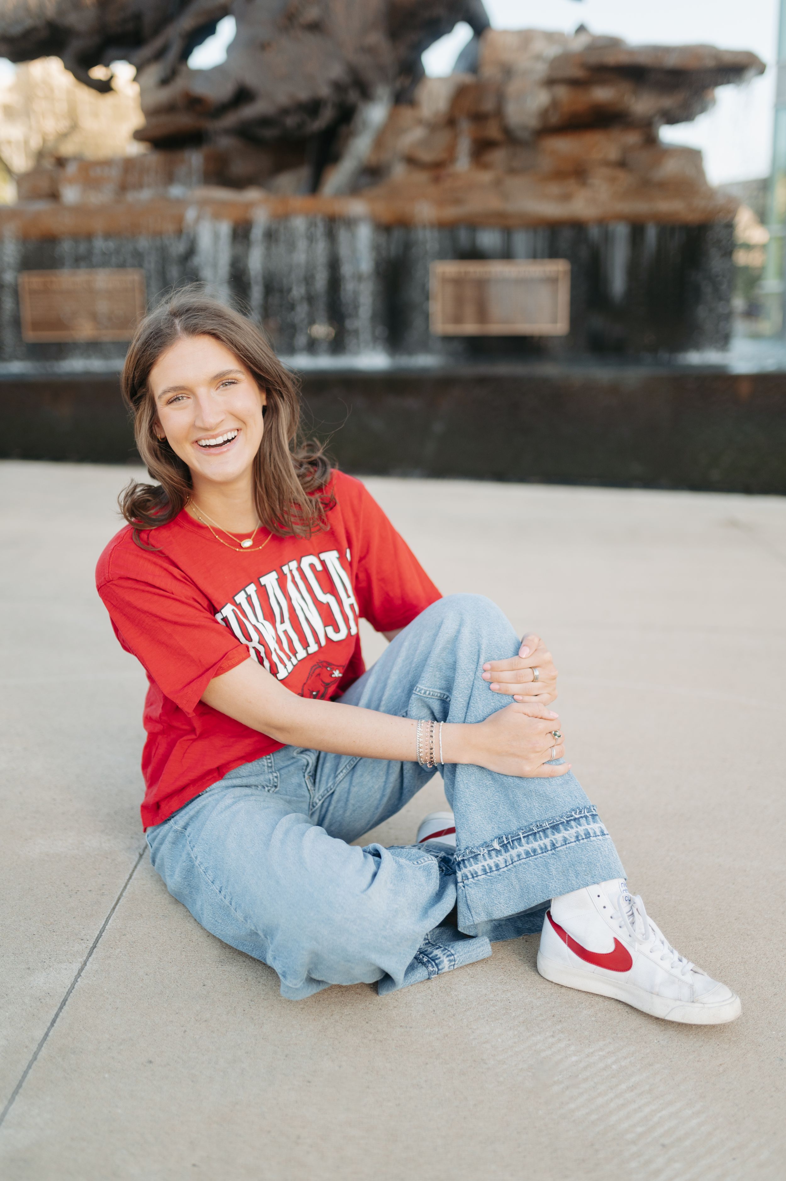 Smiling woman in red Arkansas t-shirt and jeans sitting casually in front of bronze boar fountain.