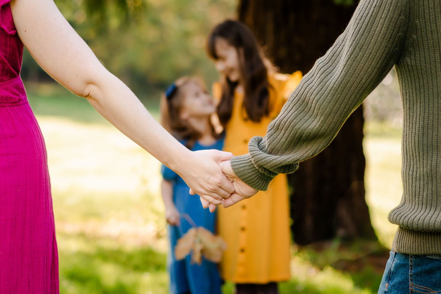 Close-up of holding hands with blurred family in background on sunny day.