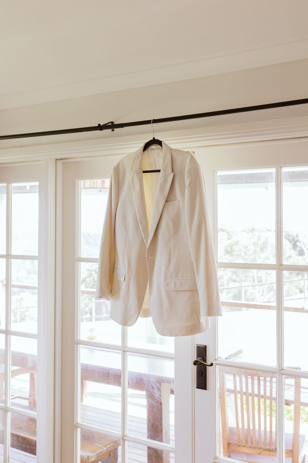 White formal jackets hanging in a row on a curtain rod against white walls and windows.
