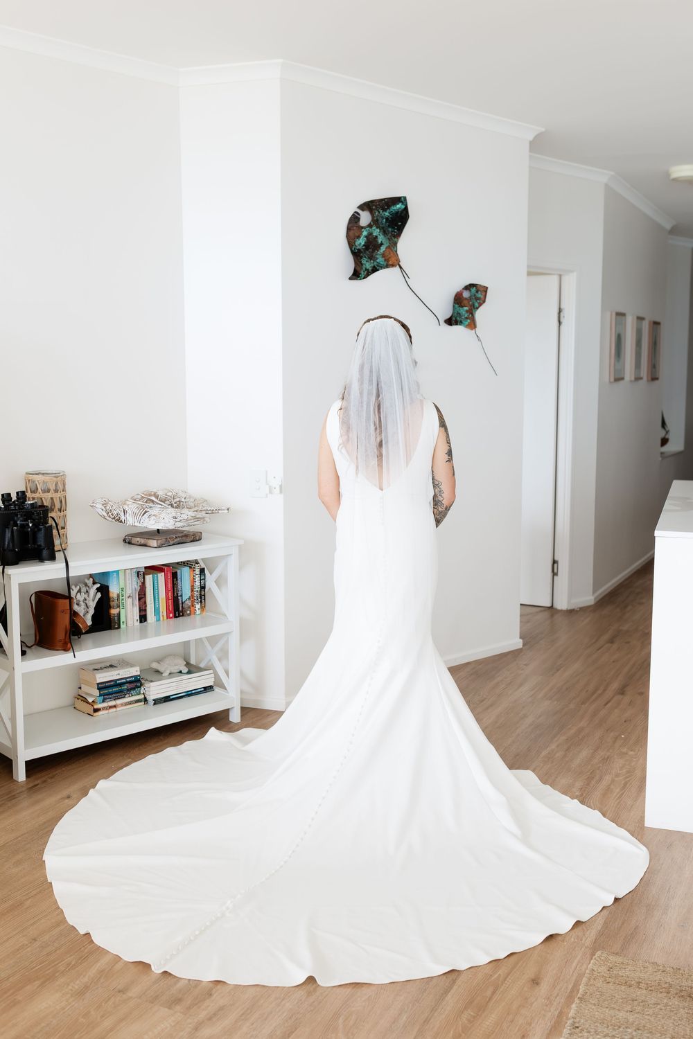 A flowing white wedding dress with a cathedral length train shown from multiple angles on a light wood floor.