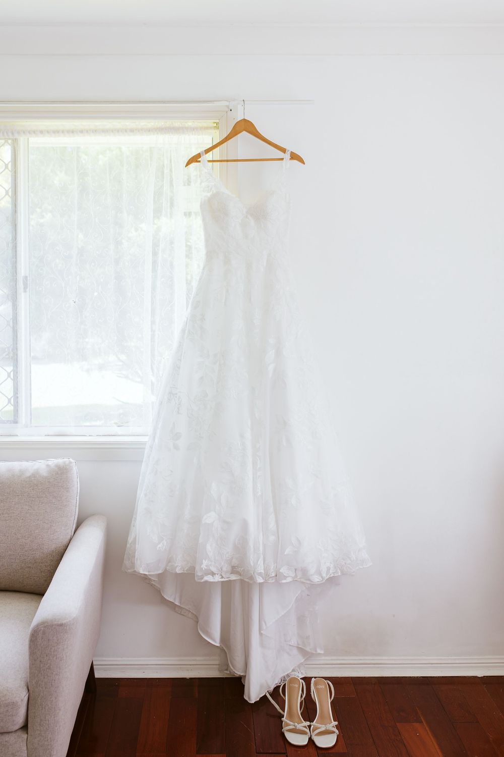 White wedding dress and shoes hanging by a window in a bright room with natural light.