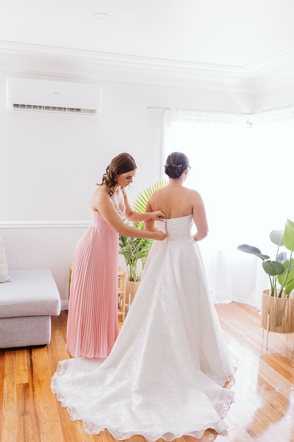 Bridesmaid in pink dress helps adjust wedding gown during final preparations.
