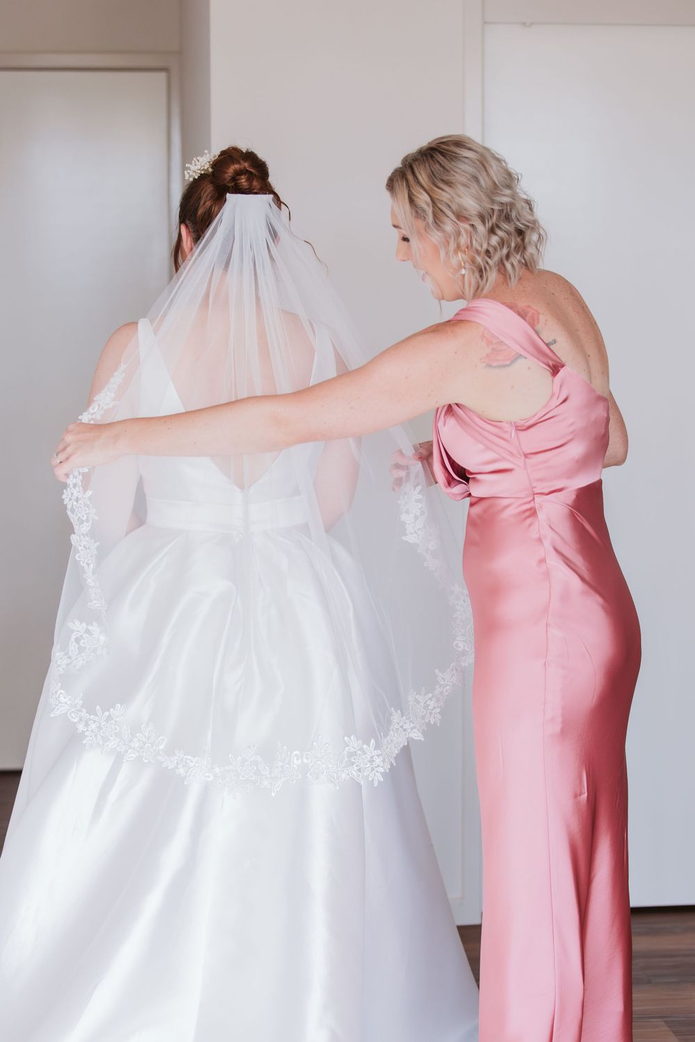 Wedding dress preparation scene with attendants in pink dresses.