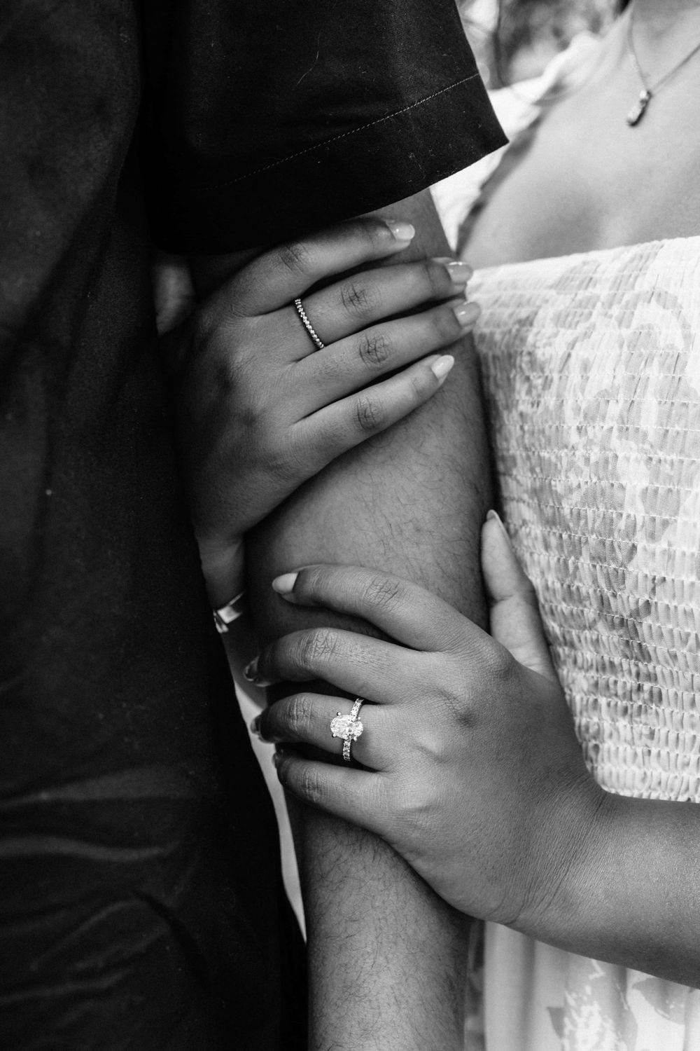 Close-up black and white photo of hands with wedding rings touching and embracing.