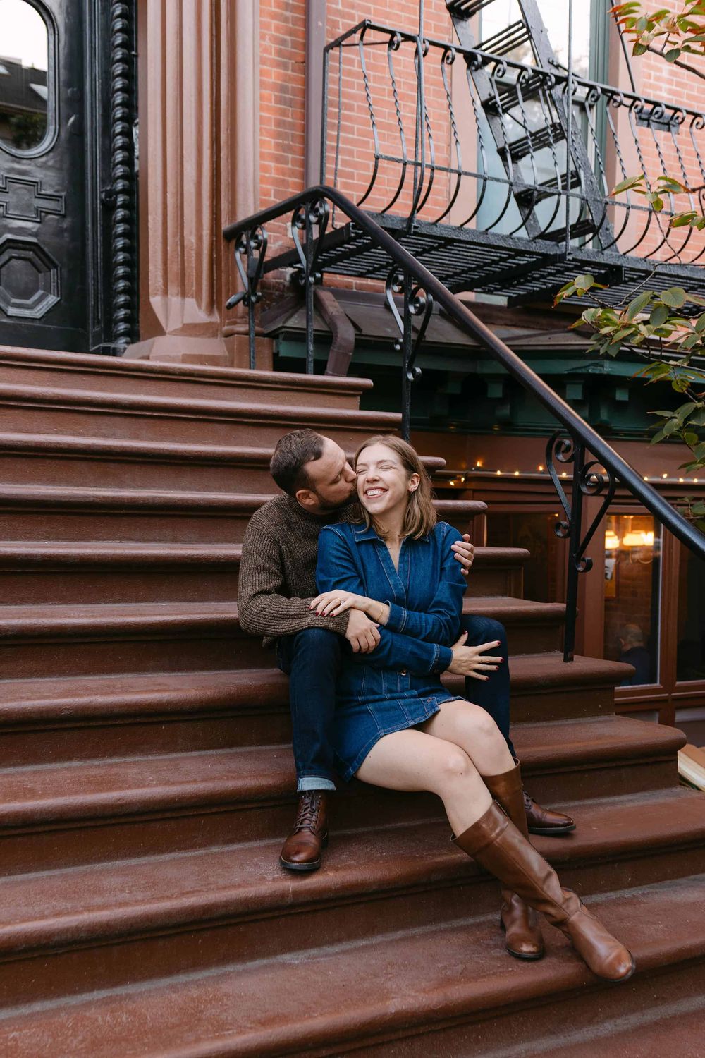 A couple shares an intimate moment while sitting on brownstone steps in front of a brick building.