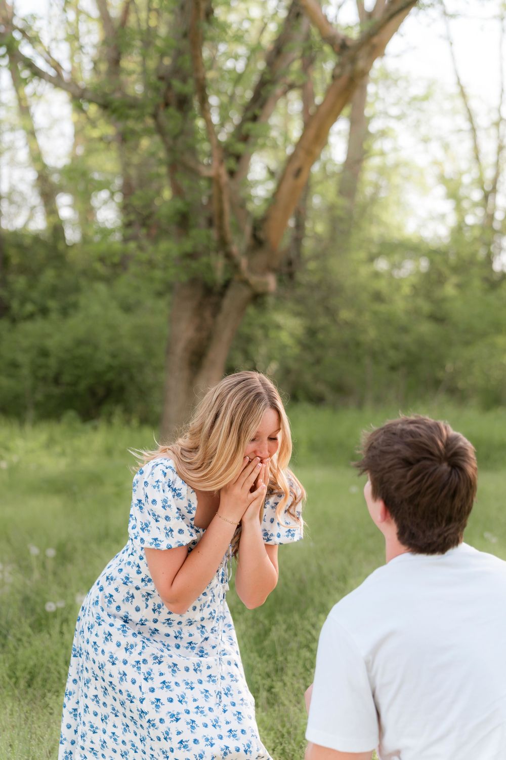 A couple shares a romantic moment in a lush green park setting as one person in a blue floral dress reacts with surprise.
