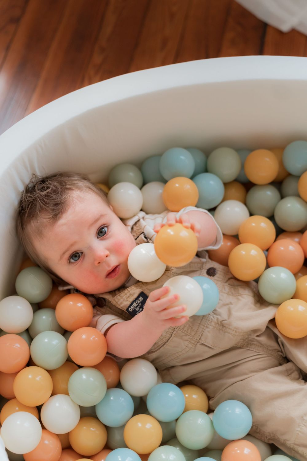 Small child laying in a ball pit filled with pastel colored plastic balls in orange, mint green, and white shades.