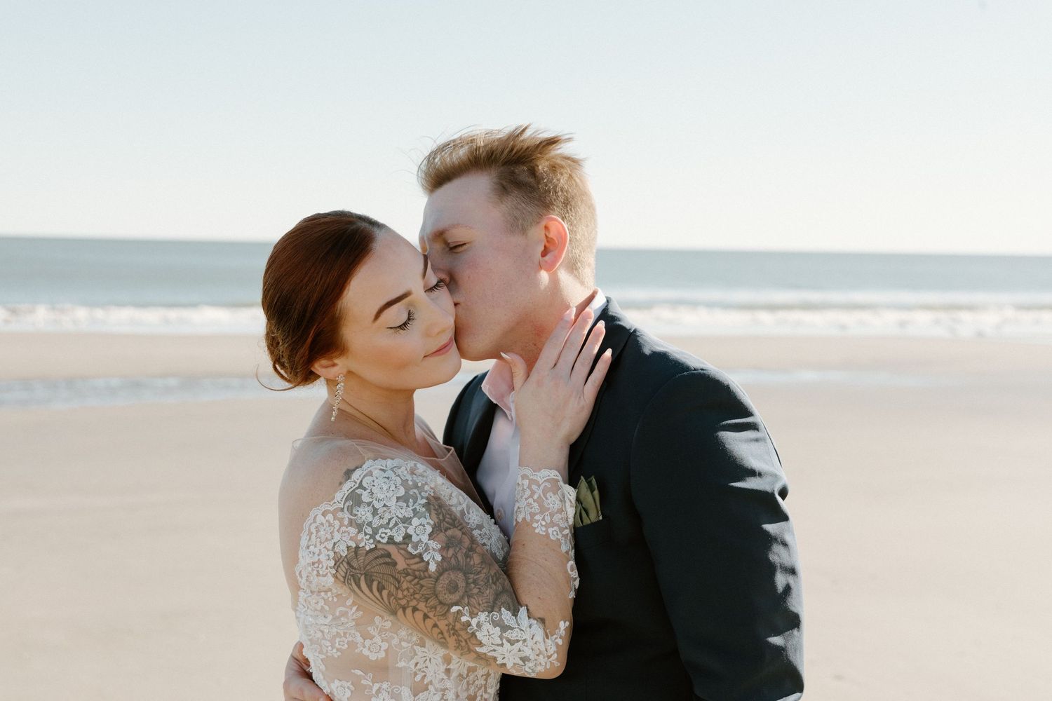 A romantic moment shared between newlyweds on a sunny beach with the bride wearing a sparkly long sleeve dress.