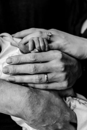 black and white close-up of Mum's, Dad's and baby's hands all touching each other