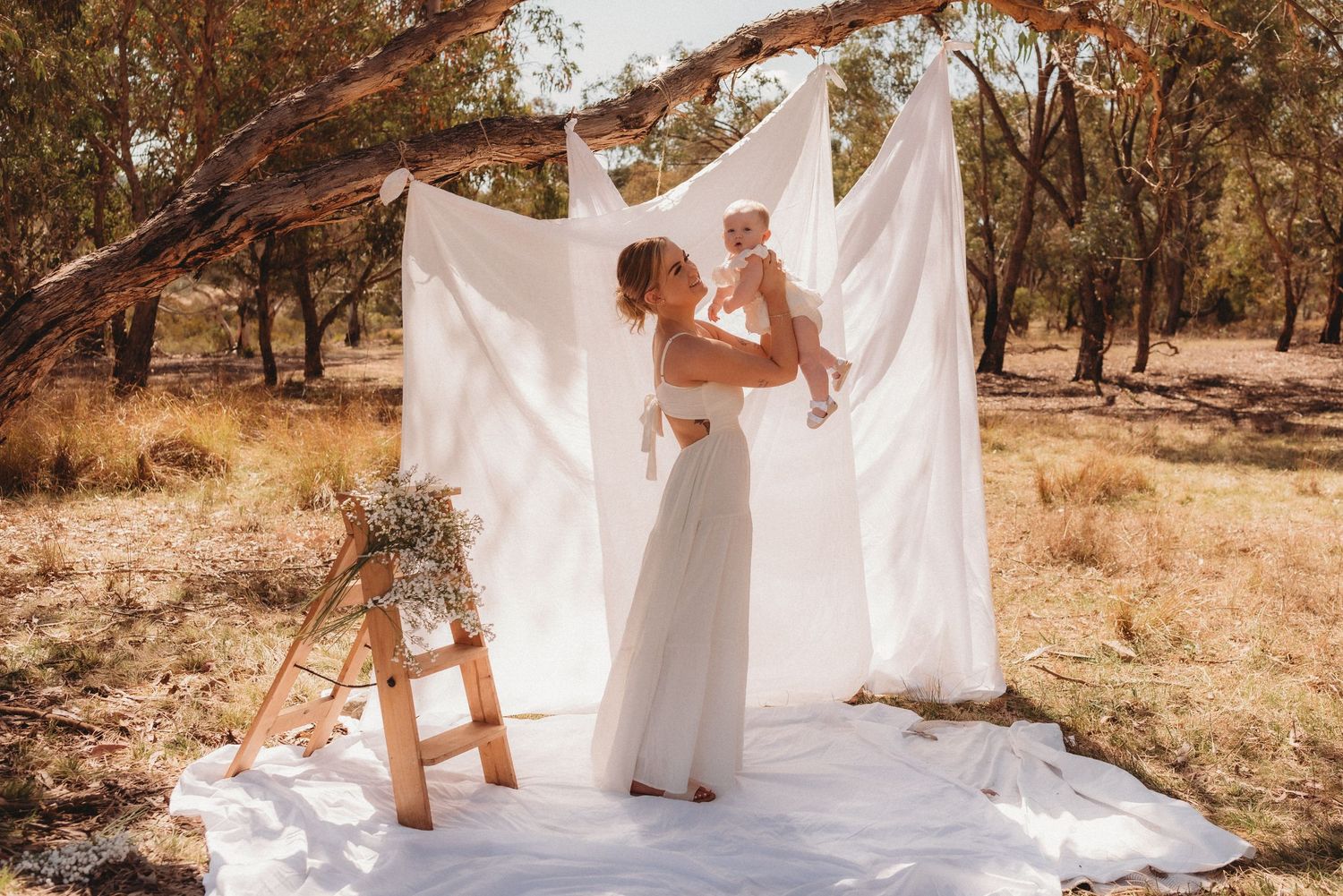 Outdoor wedding setup with white backdrop, wooden ladder, and rustic decor in autumn setting.