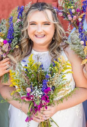 Joyful bride holds vibrant wildflower bouquet with purple and yellow blooms.